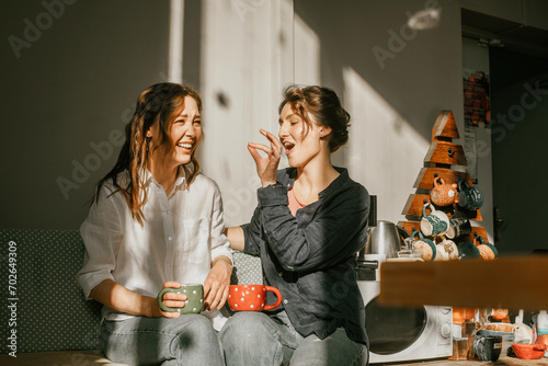 Cozy morning: girls friends talking over a cup of coffee in a bright kitchen Two women spend time peacefully on a sunny day with mugs of tea