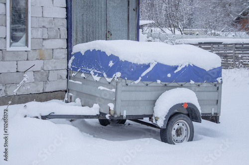A trailer for a car covered with an awning in the snow. Transportation of belongings.