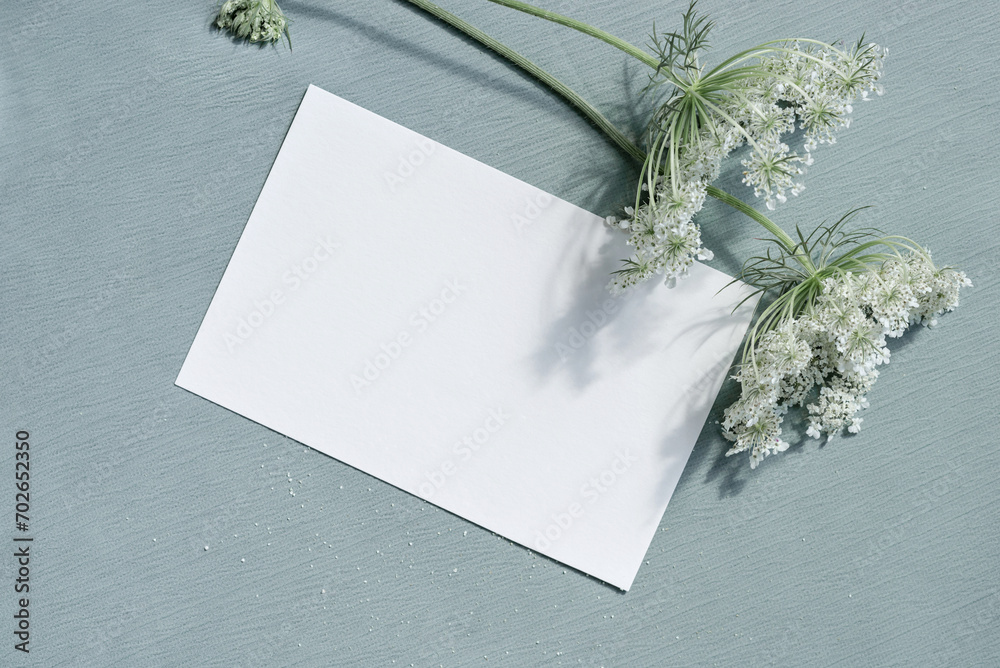Beautiful white blooming flowers and blank paper card mockup on light blue textured cloth background. Aesthetic floral greeting postcard for Mothers day, Valentines day, wedding invitation template Beautiful white blooming flowers and blank paper card mockup on light blue textured cloth background. Aesthetic floral greeting postcard for Mothers day, Valentines day, wedding invitation template