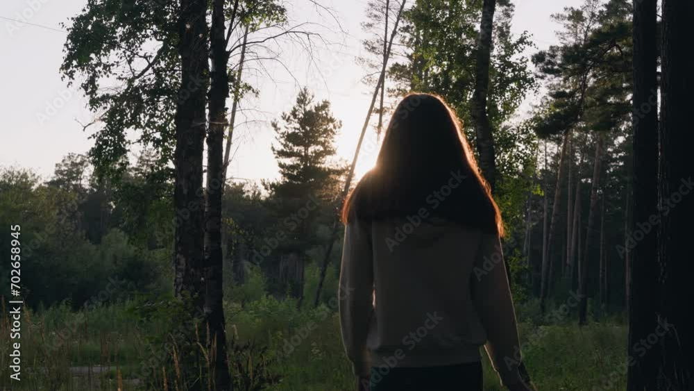 Female walking through dense woods at sunset. Young woman walks alone finding inner peace of mind in nature. Escaping from problems in fresh air