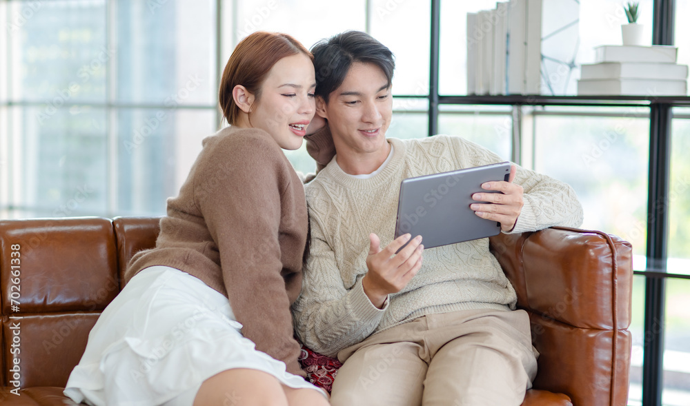 Asian young handsome male boyfriend and beautiful female girlfriend sitting smiling on sofa using tablet computer shopping online via internet together in living room at home Asian young handsome male boyfriend and beautiful female girlfriend sitting smiling on sofa using tablet computer shopping online via internet together in living room at home