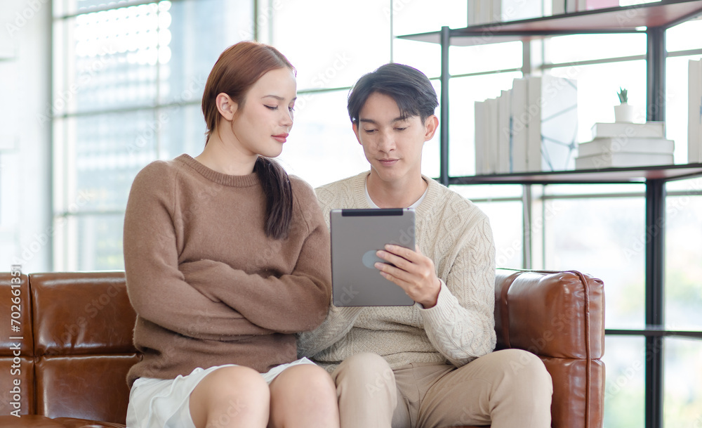 Asian young handsome male boyfriend and beautiful female girlfriend sitting smiling on sofa using tablet computer shopping online via internet together in living room at home Asian young handsome male boyfriend and beautiful female girlfriend sitting smiling on sofa using tablet computer shopping online via internet together in living room at home