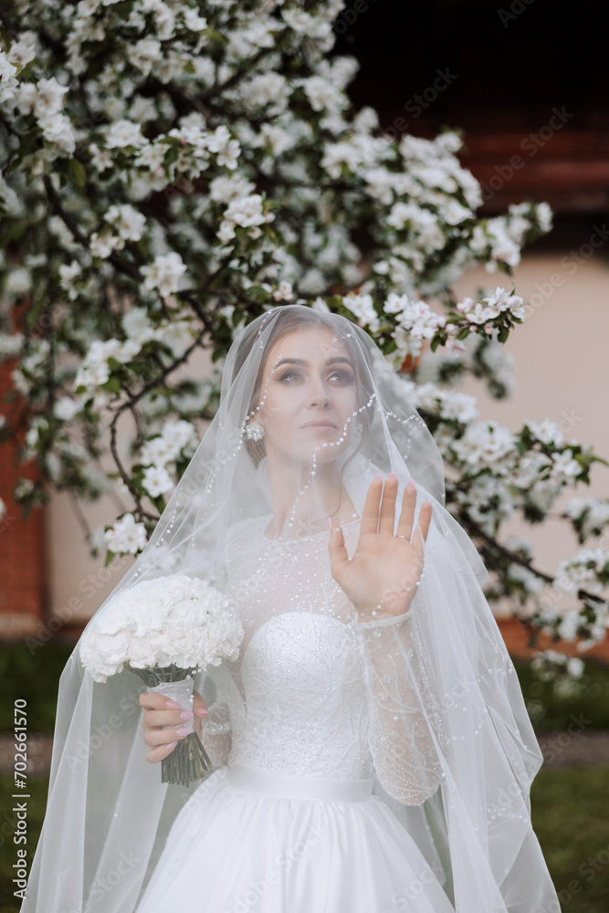 A red-haired bride poses against the background of a blooming tree. Magnificent dress with long sleeves, open bust. Spring wedding A red-haired bride poses against the background of a blooming tree. Magnificent dress with long sleeves, open bust. Spring wedding
