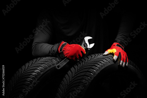 Car tires service and hands of mechanic with wrench screwdriver and sport gloves on black background.