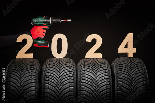 Winter car tires, tyre service, repairman hand with screwdriver for wheeels, 2024 happy new year black background photo