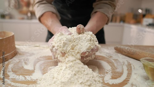 A cook in the kitchen sifts flour through a sieve. Kneading raw dough with male hands. Breaks an egg. White flour. photo