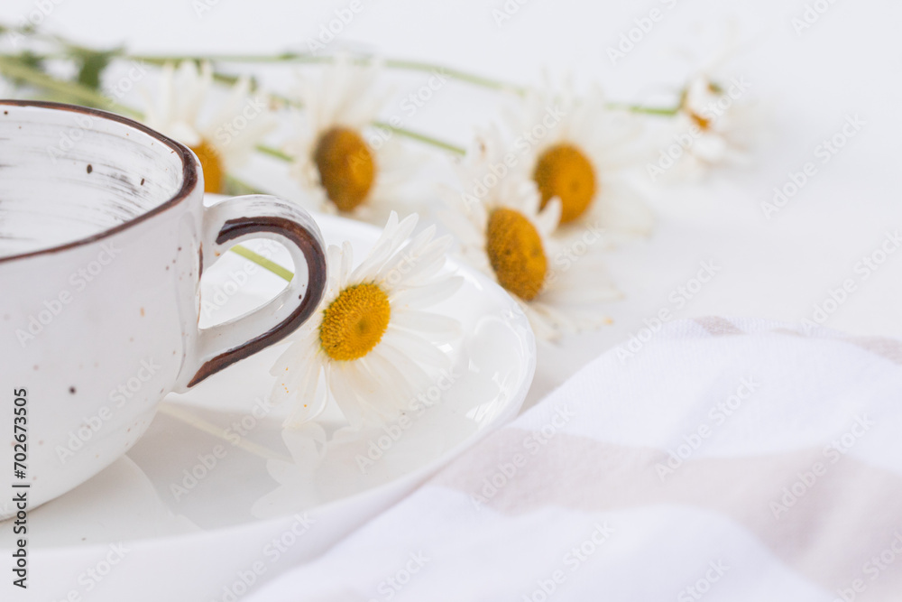 Close up of beautiful chamomile flowers and a white ceramic cup on white plate. Summer table décor, farm-style, product display or design key visual layout. Mock up, close up Close up of beautiful chamomile flowers and a white ceramic cup on white plate. Summer table décor, farm-style, product display or design key visual layout. Mock up, close up
