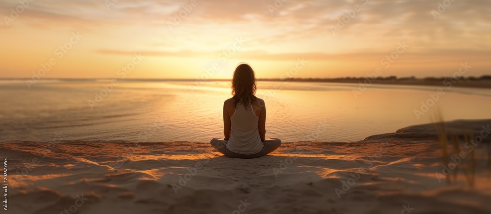 Seen from behind, female jogger relaxing on the beach at sunset meditating