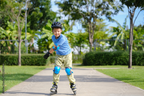 Cute little smiling Asian 7 years old child rollerblading in protection, helmet in sunny summer day © yAOinLoVE