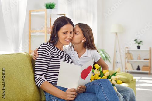 Fotografie Happy daughter showing love to mom with a surprise card and a beautiful bouquet of flowers on mother day at home