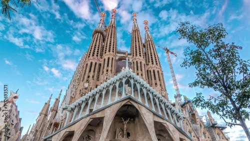 Sagrada Familia Timelapse Hyperlapse in Barcelona, Spain. The Enchanting Autumn Scene, Adorned with Green Trees Against a Picturesque Blue Cloudy Sky photo