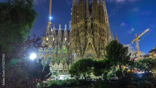 Sagrada Familia: Day to Night Transition Timelapse of the Iconic Roman Catholic Church in Barcelona, Spain. Spires and Cranes Stand Against Reflecting in the Tranquil Waters of the Nearby Lake photo