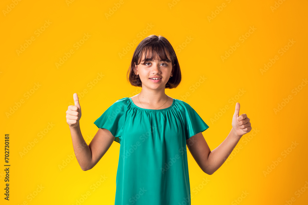 Smiling kid girl showing thumbs up gesture over yellow background. Success concept Smiling kid girl showing thumbs up gesture over yellow background. Success concept