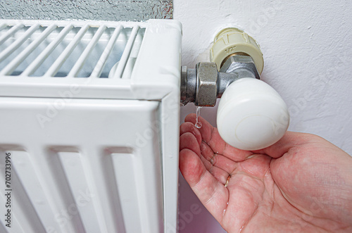 Leaking heating radiator. Defective heater. Water pours from the threaded connection of the heating pipe on the men's palm. The need for plumbing work in the heating period at home. photo