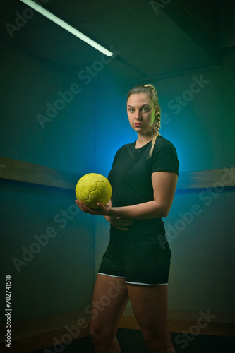 Female handball player stands in the locker room in coloured light holding a ball  © AstrorickyPhotograpy