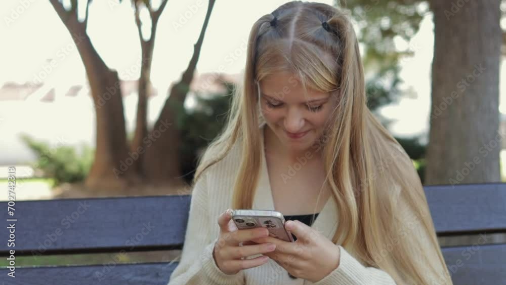 Happy beautiful teenager girl holding cell phone using educational apps and looking at text messages on smartphone standing outside. Online mobile applications concept. High quality FullHD footage Happy beautiful teenager girl holding cell phone using educational apps and looking at text messages on smartphone standing outside. Online mobile applications concept. High quality FullHD footage