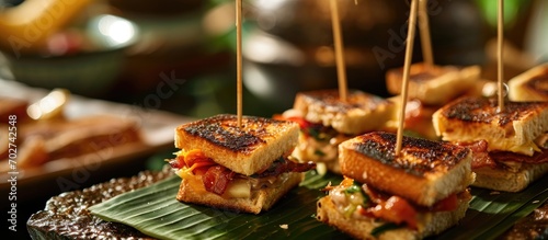 Restaurant service featuring bite-sized grilled cheese and bacon sandwiches on bamboo toothpicks and banana leaf garnish. photo