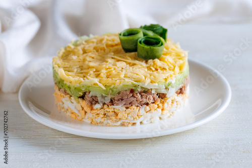 Layer canned tuna, fresh cucumber, boiled egg and cheese salad on white plate on a table. Selective focus. Side view, close up