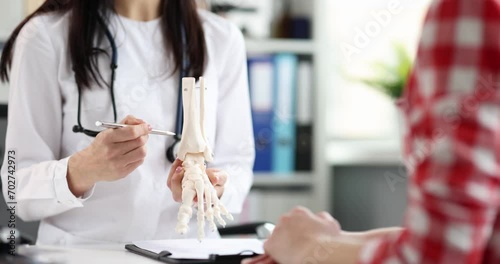 Doctor traumatologist shows model of a plastic leg of person to patient with problem with feet. Foot anatomy and skeleton concept photo