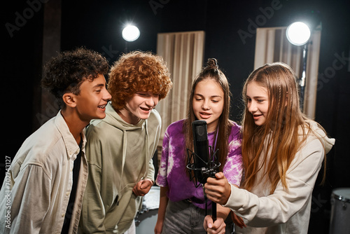 four joyous talented teenagers in casual outfits singing together while in studio, musical group