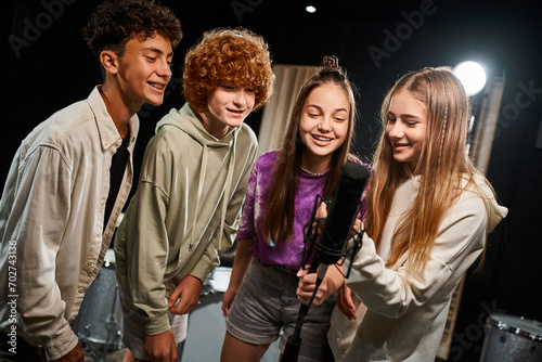 cheerful cute teenagers in everyday vibrant attires singing together into microphone, musical group