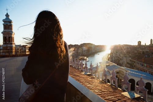 A young woman enjoys alone a charming sunset as the breeze lifts her hair from a terrace overlooking the Grand Canal in Venice, Italy
