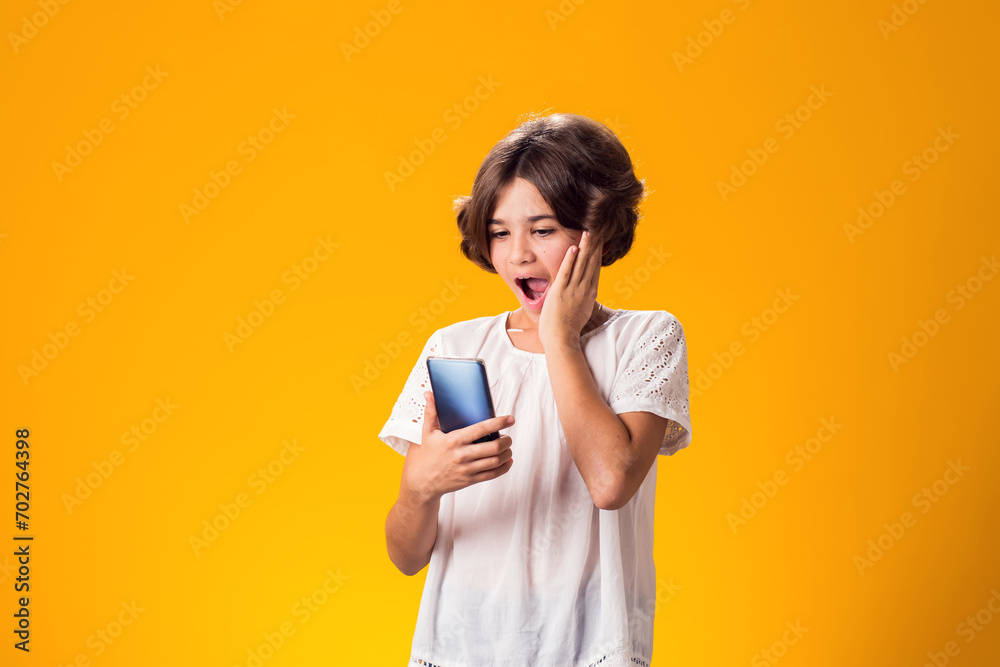 Surprised kid girl holding smartphone in hand over yellow background Surprised kid girl holding smartphone in hand over yellow background
