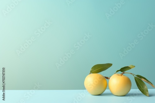  a couple of yellow apples sitting on top of a table next to a green leafy branch on a light blue background.