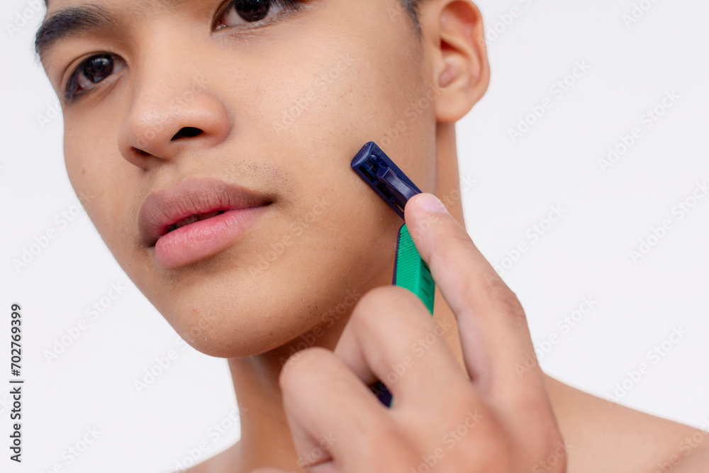 A young asian man using a disposable razor to cleanly shave the sideburns. Closeup tight shot isolated on a white backdrop.