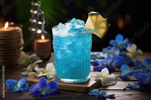  a blue drink sitting on top of a wooden table next to blue flowers and a lit candle in the background.