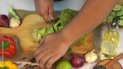 Woman's hand slicing fresh broccoli on wooden chopping board