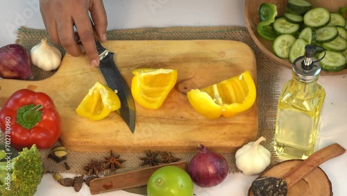 Chopping yellow bell pepper for salad on wooden cutting board