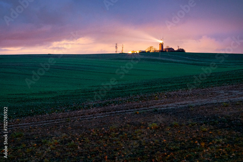 Ein Leuchtturm nach Sonnenuntergang   ber einem Feld mit spektakul  rem Himmel.