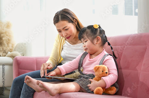 young asian female using tablet with her kid,mother spend free time on weekend together with a little daughter in the living room