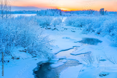 Winter frosty landscape. Landscape with river and snowy forest in Western Siberia. Freezing river against sunset background.