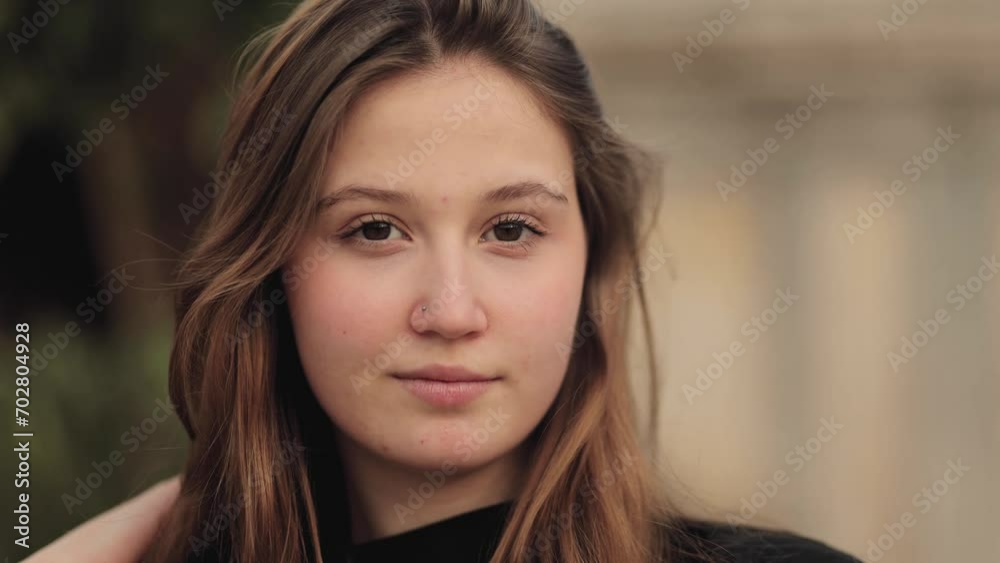 A very beautiful and expressive girl model, student looks directly into the camera, maintaining eye contact and smiling. Close portrait, people, fashion and beauty. Cinematic shot.