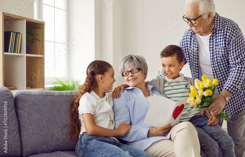 It's time for birthday gifts. Happy grandmother receives birthday presents from her loving family. Children together with grandfather give grandma a card and a bouquet of beautiful flowers