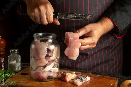 The cook preserves fresh carp fish in a jar with spices. The chef hands hold a fish steak and a knife. Working environment in a restaurant kitchen. photo