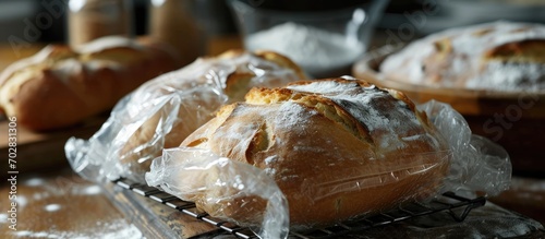 Loaves of thick white bread wrapped in clear plastic bags on a wire rack There are scoured shapes such as a heart on the top of the fresh crusty sourdough baked bread There s white flour on the