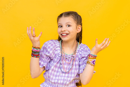 The young girl put on a lot of beaded jewelry. Beading for children and teenagers. Portrait of a little girl. Beaded bracelets. Yellow isolated background.