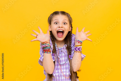 The happy little girl opened her mouth wide with delight and spread her fingers in different directions. The child dressed up in colorful beaded bracelets. Beading for children and teenagers. photo