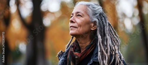 Thoughtful senior woman with dreadlocks standing outdoors in casual attire.
