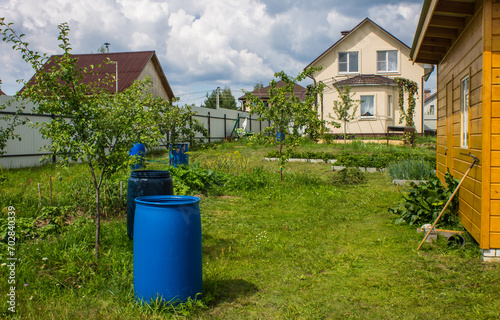 Plastic barrel and watering can in the garden among trees and green grass on a sunny summer day. Concept gardening and plant care in rural areas