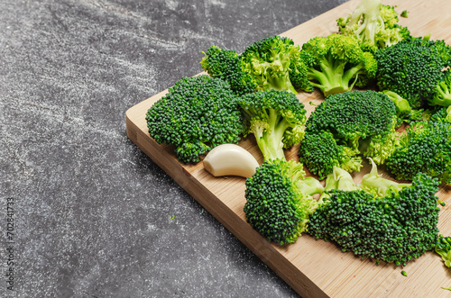 Broccoli florets and garlic cloves on wooden board. Dark background. Simple ingredients for health.