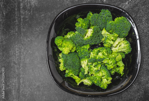 Fresh green broccoli florets in black bowl isolated on gray background, top view.