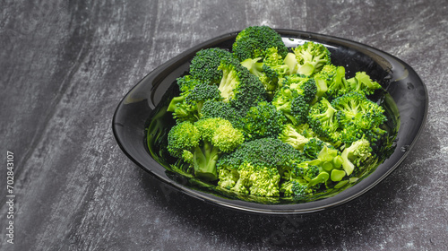 Fresh green broccoli florets in black bowl isolated on gray background, side view.