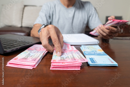 Close up of man's hands counting Indonesian rupiah notes and making notes, money financial management concept. Soft focus, Selective focus