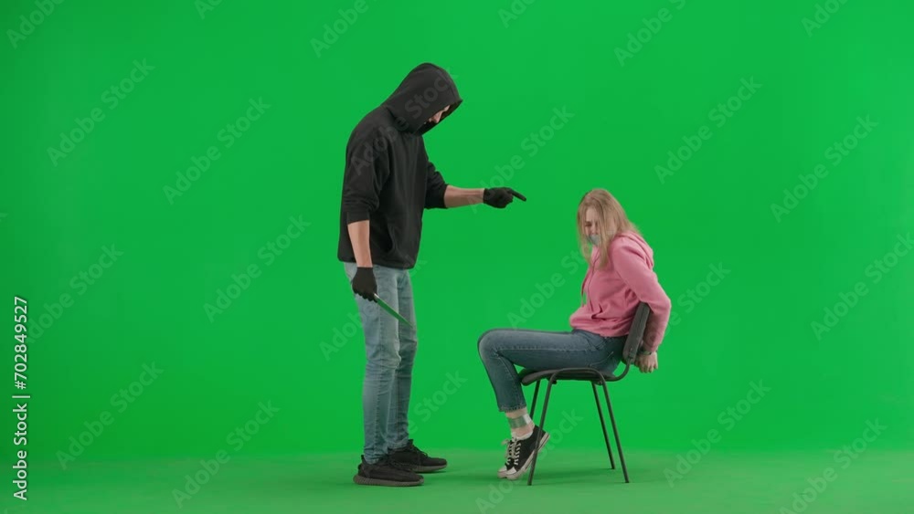 Portrait of thief and victim on chroma key green screen background. Girl sitting on chair tied hands and taped mouth man robber with knife threatens her. Portrait of thief and victim on chroma key green screen background. Girl sitting on chair tied hands and taped mouth man robber with knife threatens her.
