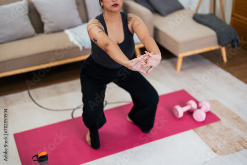 Overweight woman enjoying a fitness workout at home. Fat, plump woman and squatting on an exercise mat in the living room