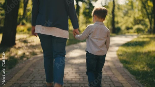 Grandmother and little grandson holding hands, walking together in sunny park photo